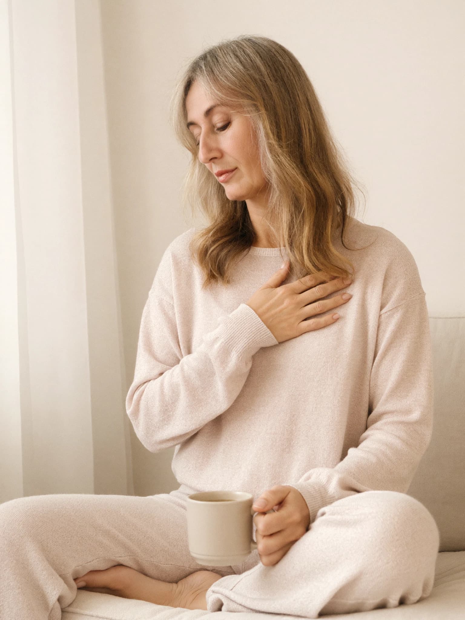 Teri sitting quietly with a cup of tea, one hand resting on her heart